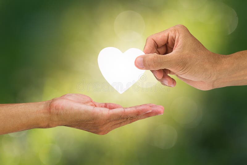 Hand holding and giving white heart to receiving hand on blurred green bokeh background stock image Hand holding and giving white heart to receiving hand on blurred green bokeh background stock image