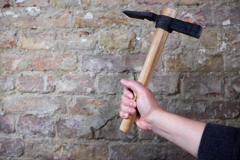 A Hand Holding Hammer Against Brick Wall with Copy Space Stock Image