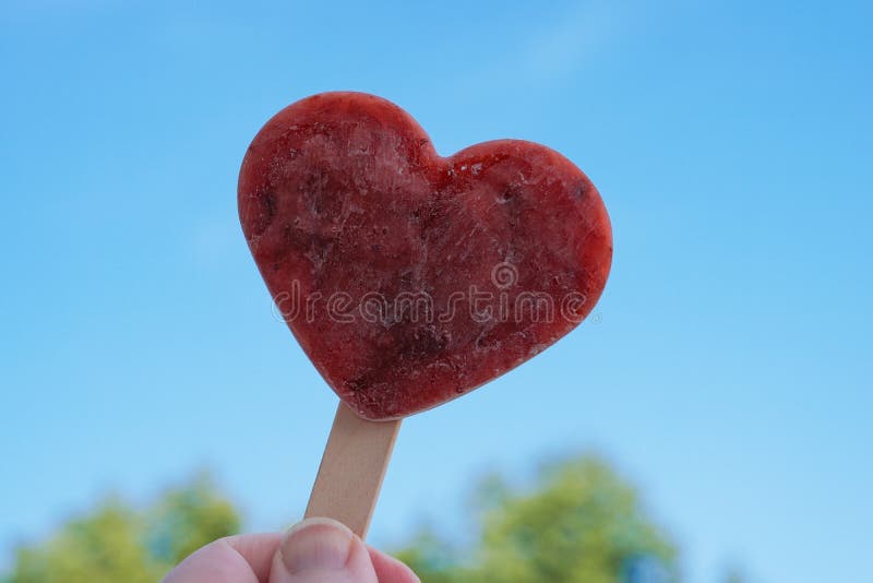 Hand holding heart shaped homemade berry popsicle or ice lolly against clear blue sky - love summer concept. Hand holding heart shaped homemade berry popsicle or ice lolly against clear blue sky - love summer concept