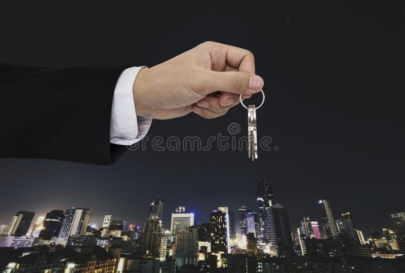 Hand holding keys with city background, real estate and property concept