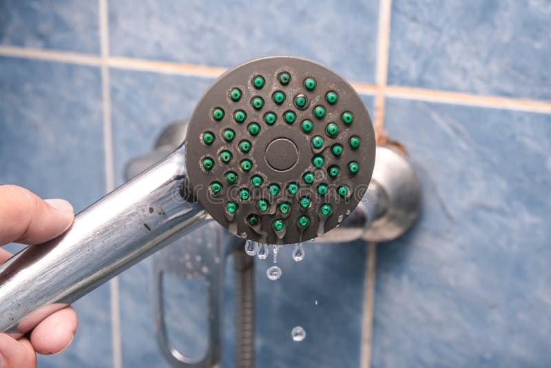 Hand holding leaking, dropping dirty calcified shower head, clogged nozzles, injectors with limescale stock photo
