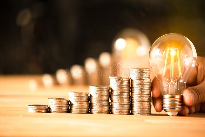 Hand holding a light bulb with coins stack royalty free stock images