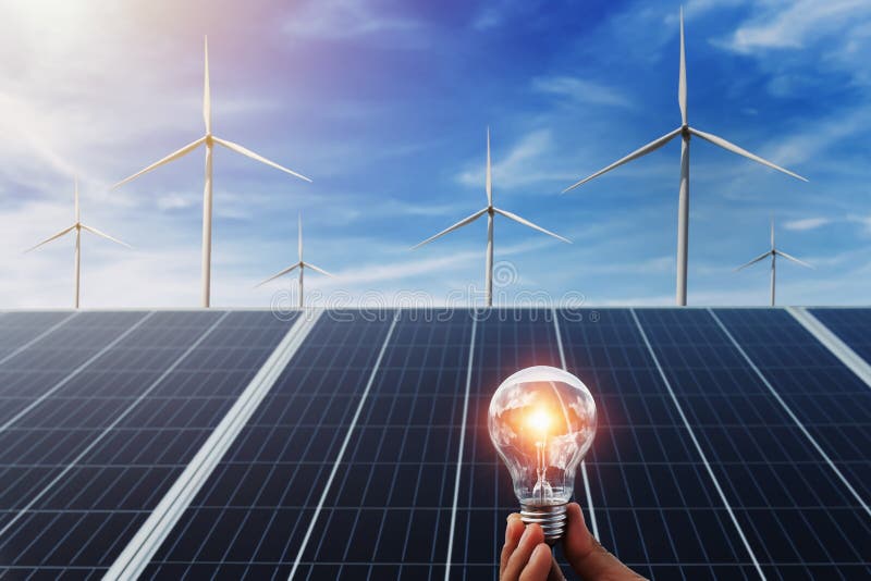 hand holding lightbulb with solar panel and wind turbine background. clean energy in nature concept