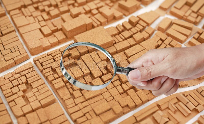 Hand holding Magnifying glass on the cork architecture small city model dummy