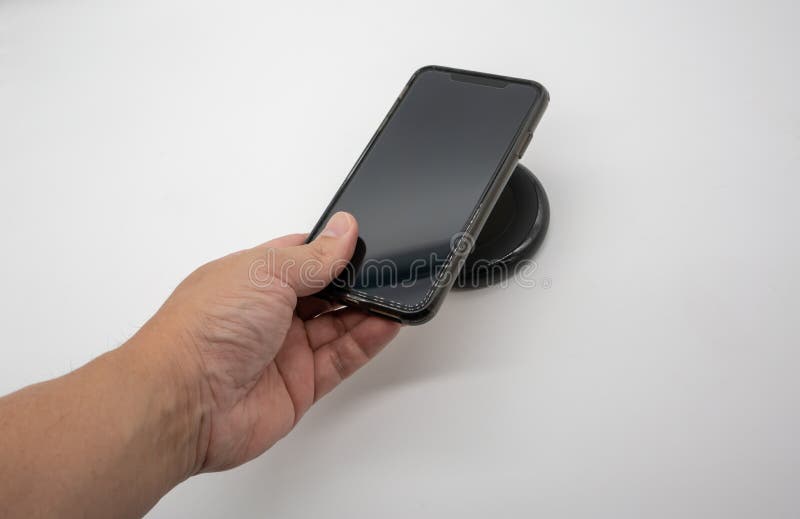 Hand holding mobile phone over black wireless charger o royalty free stock photography Hand holding mobile phone over black wireless charger o royalty free stock photography