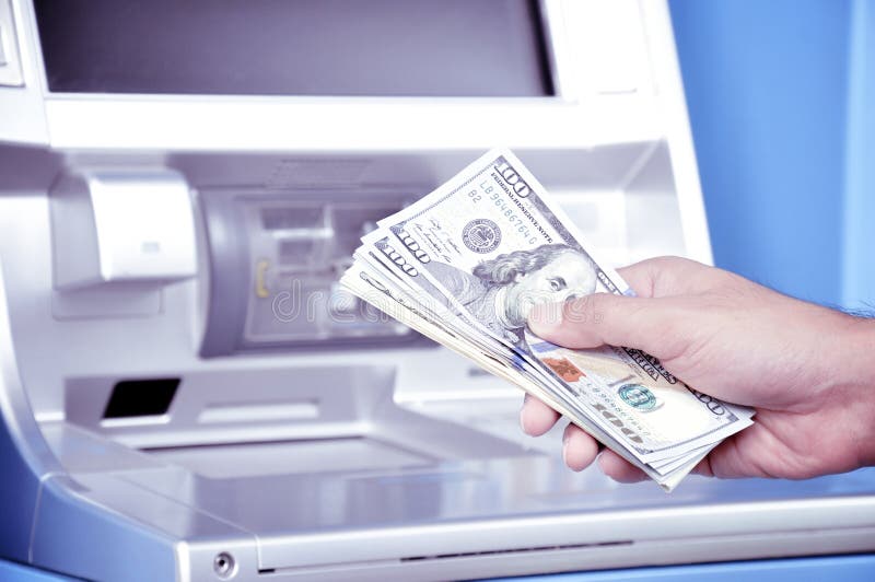 Hand holding money United States dollar (USD) banknotes in front of ATM