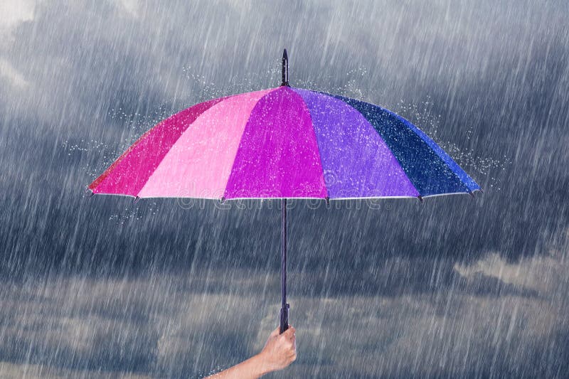 Hand holding multicolored umbrella under dark sky with rain stock photography