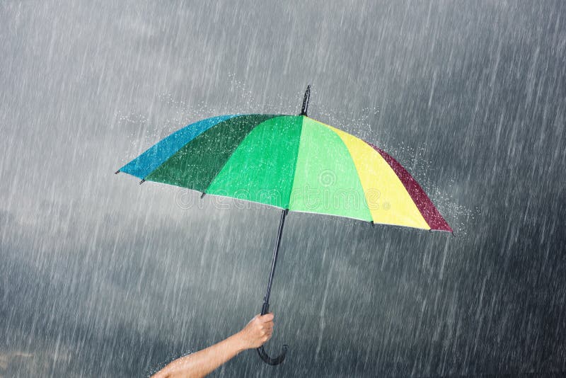 Hand holding multicolored umbrella under dark sky with rain royalty free stock photo