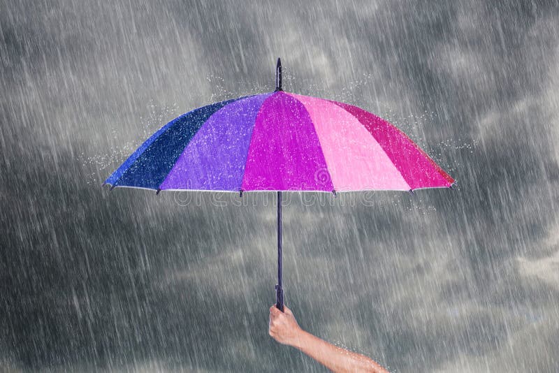 Hand holding multicolored umbrella under dark sky with rain royalty free stock images