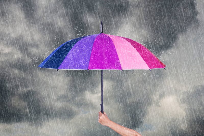 Hand holding multicolored umbrella under dark sky with rain stock image