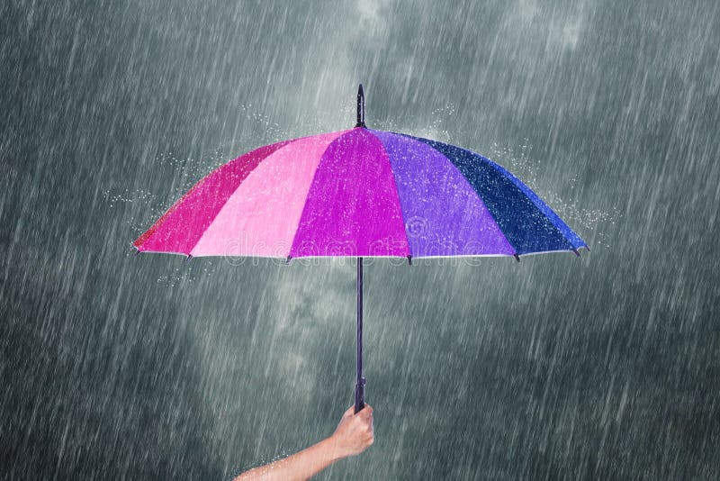 Hand holding multicolored umbrella under dark sky with rain royalty free stock image