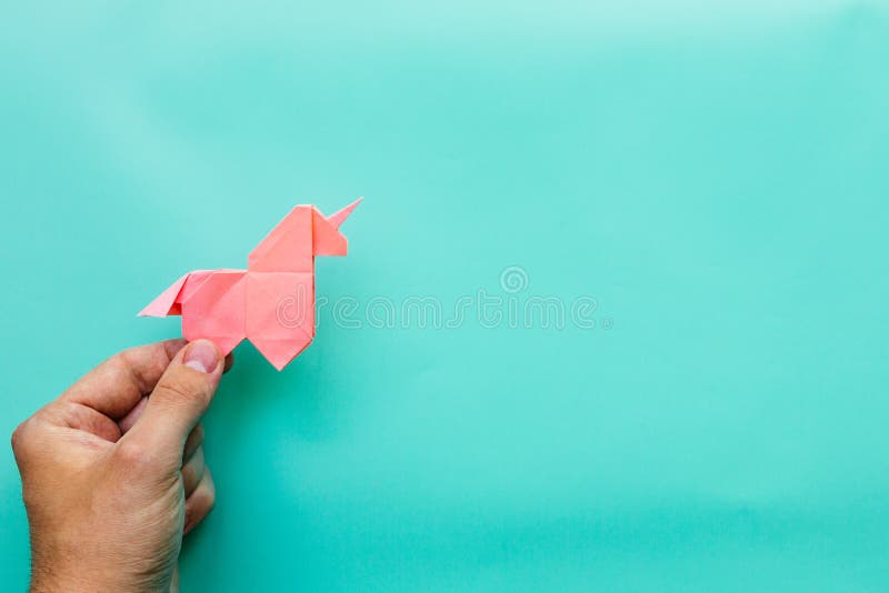 Pink origami unicorn on cyan blue background