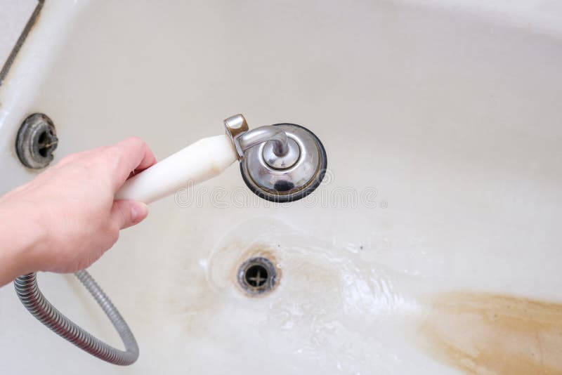 A hand holding shower head with running water against rusty bathtube with limescale, bathroom clining and decalcifying royalty free stock photos