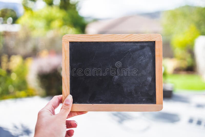 Hand holding small blackboard with blank copy space in front of stylish backyard patio background stock photography Hand holding small blackboard with blank copy space in front of stylish backyard patio background stock photography