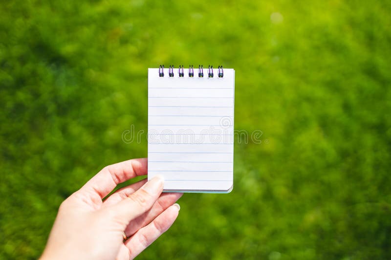 Hand holding small notebook with blank copy space in front of perfect green grass lawn royalty free stock photography Hand holding small notebook with blank copy space in front of perfect green grass lawn royalty free stock photography