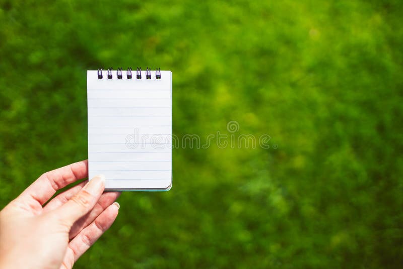 Hand holding small notebook with blank copy space in front of perfect green grass lawn stock photo Hand holding small notebook with blank copy space in front of perfect green grass lawn stock photo