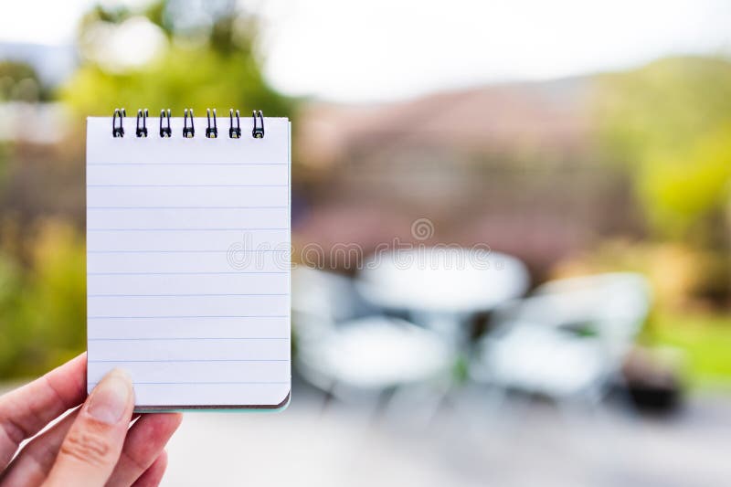 Hand holding small notepad with blank copy space in front of stylish backyard patio background royalty free stock photo Hand holding small notepad with blank copy space in front of stylish backyard patio background royalty free stock photo