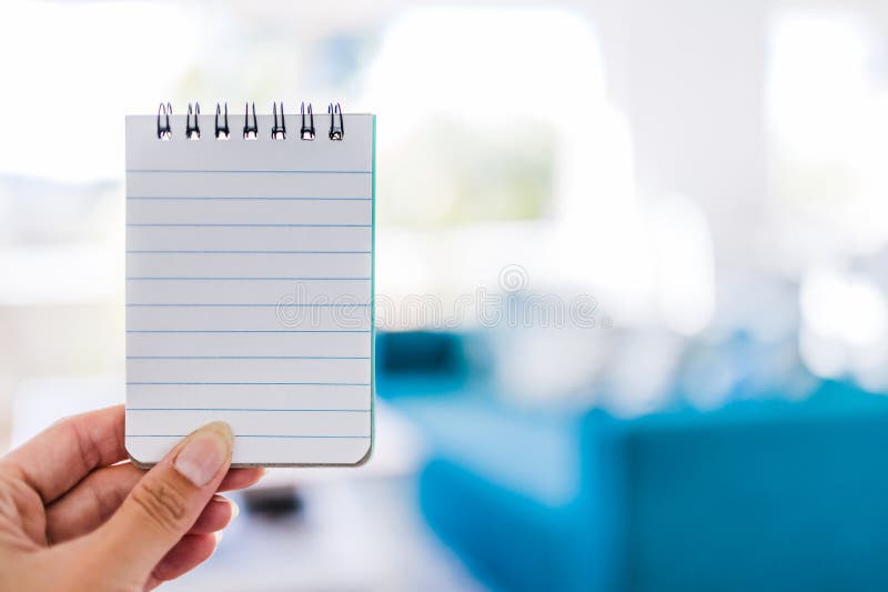 Hand holding small notepad with blank copy space in front of stylish living room background royalty free stock photography Hand holding small notepad with blank copy space in front of stylish living room background royalty free stock photography