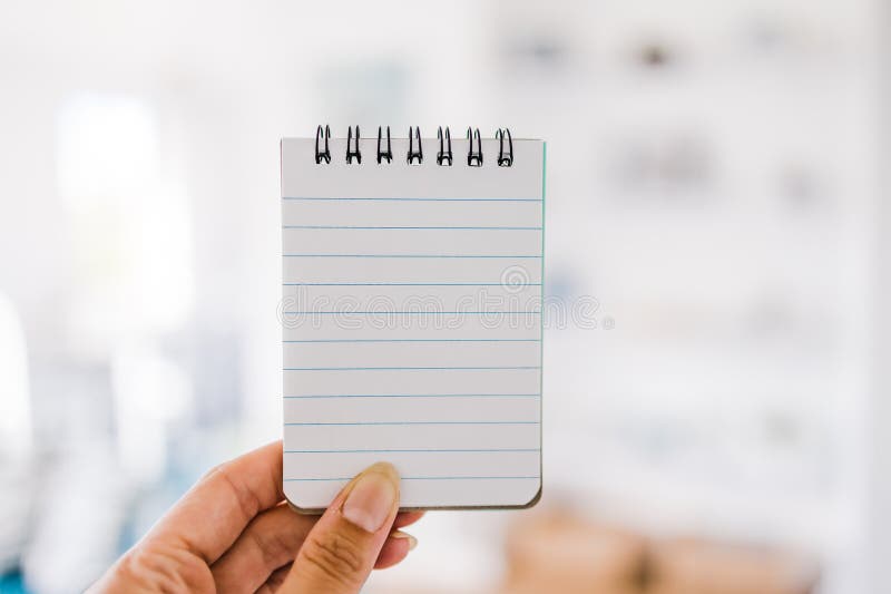 Hand holding small notepad with blank copy space in front of stylish living room background royalty free stock photography Hand holding small notepad with blank copy space in front of stylish living room background royalty free stock photography