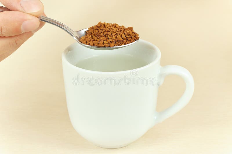 Hand Holding a Spoon with Granulated Coffee Over Cup of Water Stock