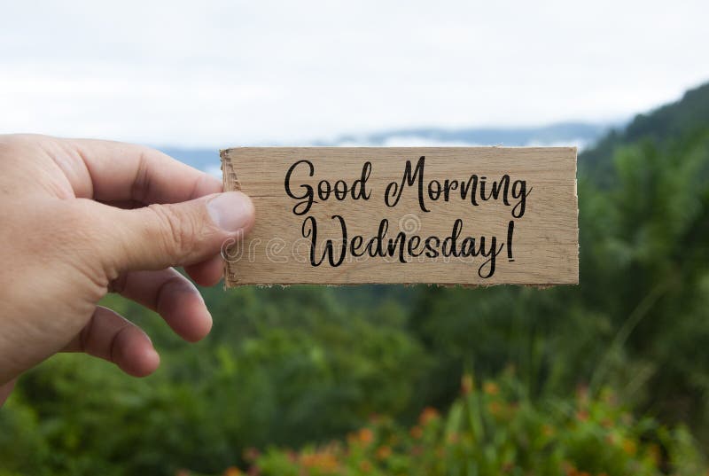 Hand holding wooden banner with Good Morning Wednesday text. With beautiful nature background. Morning wishes concept.