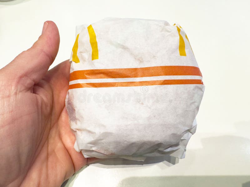 Hand holding wrapped fast food burger on white surface royalty free stock photography