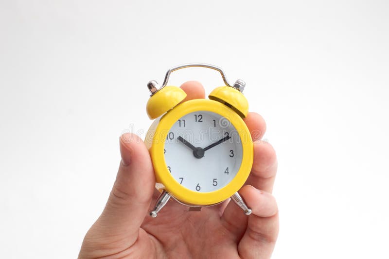 Hand Holding Yellow Alarm Clock on Light Background. Time Concept Stock