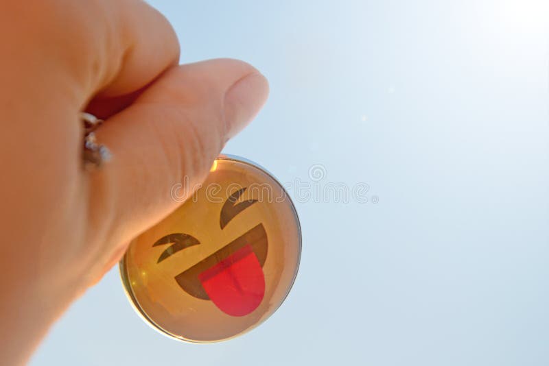 The hand holds a yellow keychain against the background of a sunny blue clear sky. Smile shows tongue, carefree joyful life stock photography The hand holds a yellow keychain against the background of a sunny blue clear sky. Smile shows tongue, carefree joyful life stock photography