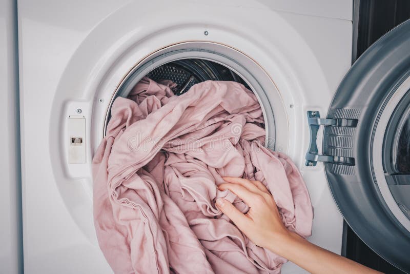 A Hand Inserting Soft, Pink Bedding Into a Modern Washing Machine for Fresh Laundry Cleaning and Care royalty free stock photo