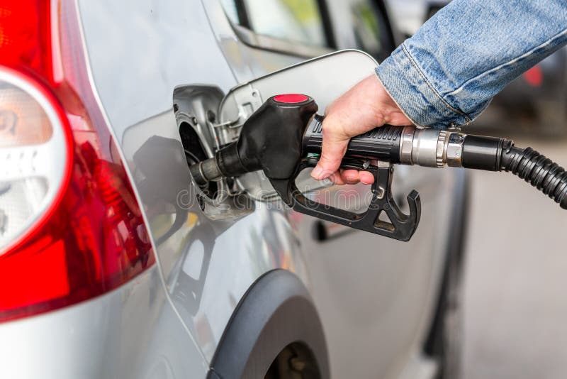 Hand in jeans jacket refueling gray metallic car on gas station - closeup with selective focus