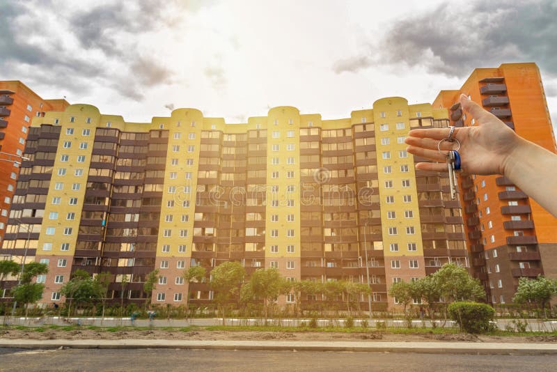 A Hand with the Keys To an Apartment on the Background of an Apartment Building in the Rays of