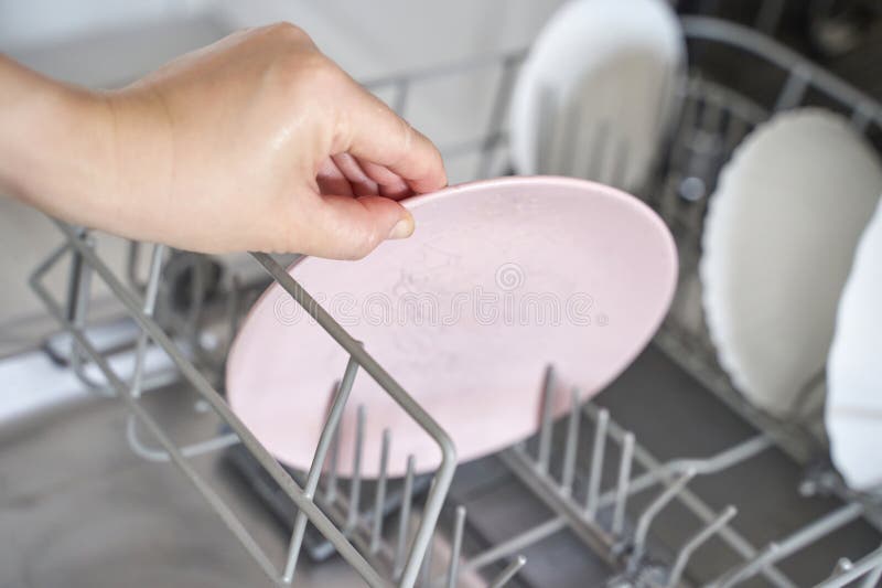 Hand loading pink dish in dishwasher close up view of kitchen appliance use. Automatic loading stock images, royalty-free photos and pictures