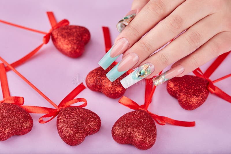 Hand with long artificial manicured nails colored with white and turquoise nail polish and red hearts Valentine day decor