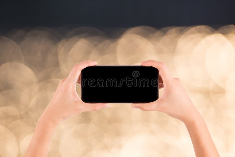 Hand med mobiltelefonen på ljus skinande bokehbakgrund arkivbilder