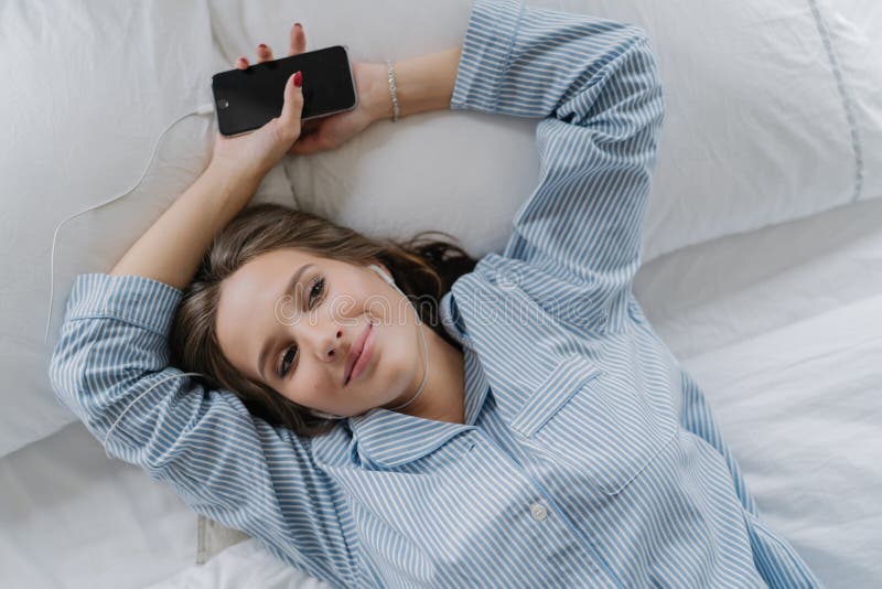 Hand met polshorloge in een zak Het mooie meisje met tevreden tevreden uitdrukking, gekleed in pyjama, rust in bed, houdt slimme royalty-vrije stock fotografie Hand met polshorloge in een zak Het mooie meisje met tevreden tevreden uitdrukking, gekleed in pyjama, rust in bed, houdt slimme royalty-vrije stock fotografie