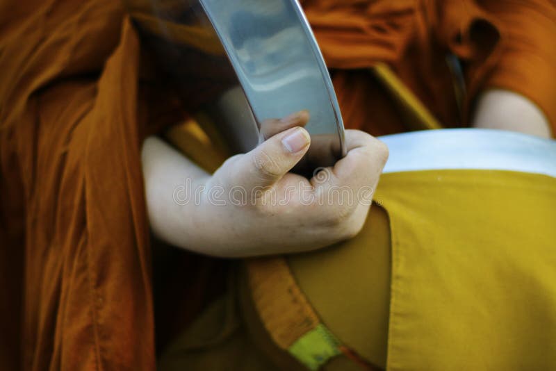 Hand of monk dressing orange robe, holding bowl during reception of alms royalty free stock photography