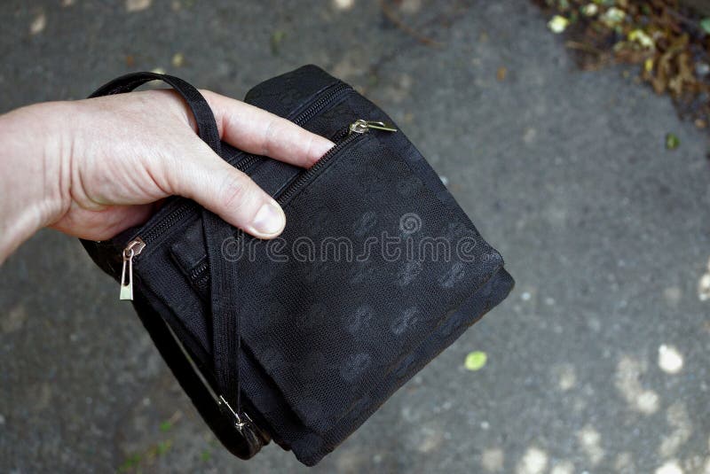 Hand in an open small black bag on the street