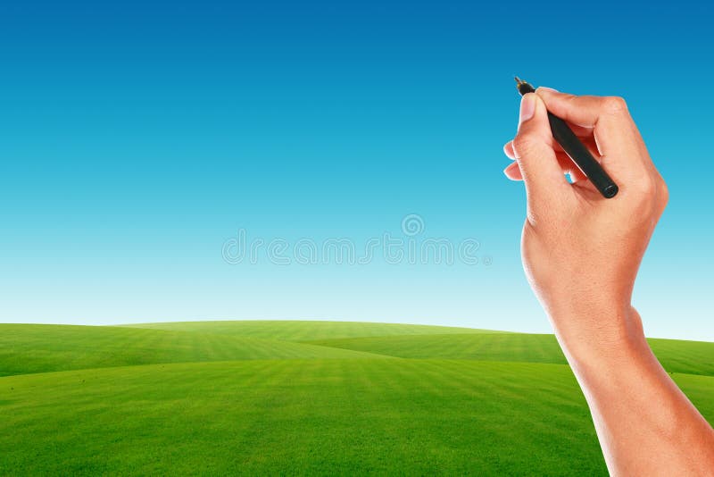Hand with pen on blue sky and green grass field