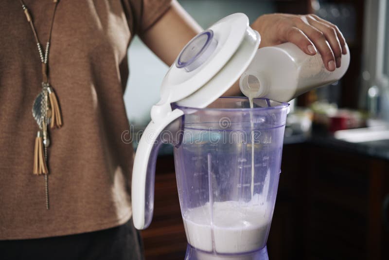 Making milkshake. Hand of person pouring milk into mixer to make delicious healthy cocktail stock photos