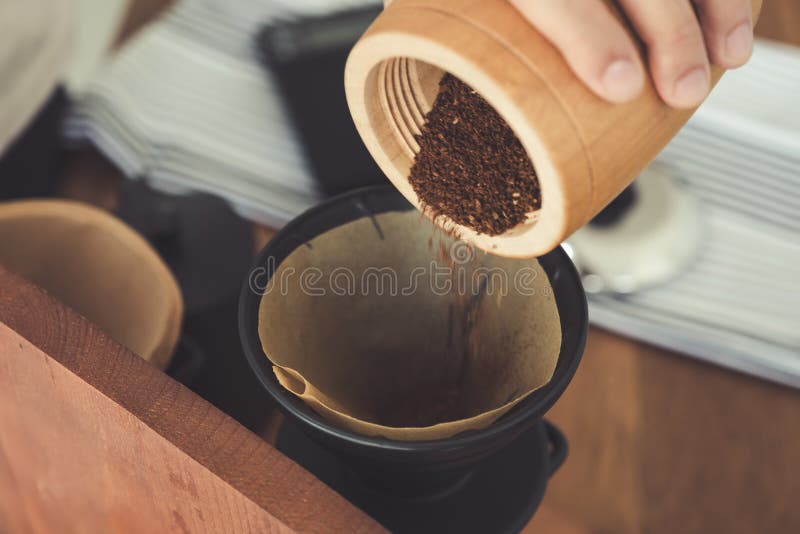A Hand Pouring Coffee from Wooden Grinder into a Drip Coffee Filter