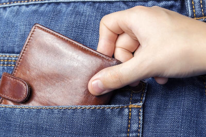 A hand pulls a wallet out of the back pocket of his jeans.The concept of pickpocketing or theft in the family from parents.Close