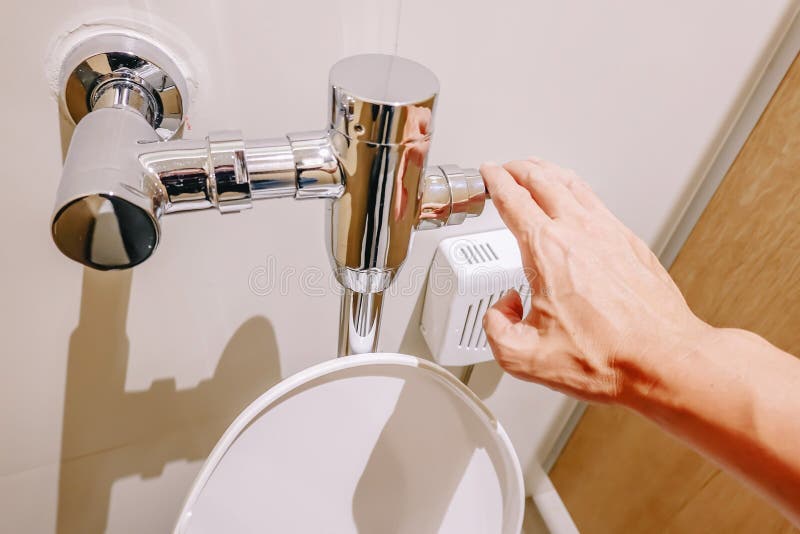 Hand pushing button and flushing urinal cleaning toilet in restroom