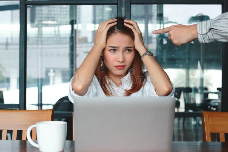 Hand`s boss pointing anxious depressed Asian business woman in office.