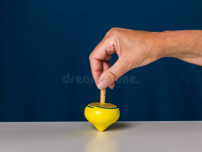 Hand of senior woman holding wooden yellow spinning top, close-up, dark blue background. Hand of senior woman holding wooden yellow spinning top, close-up, dark blue background.