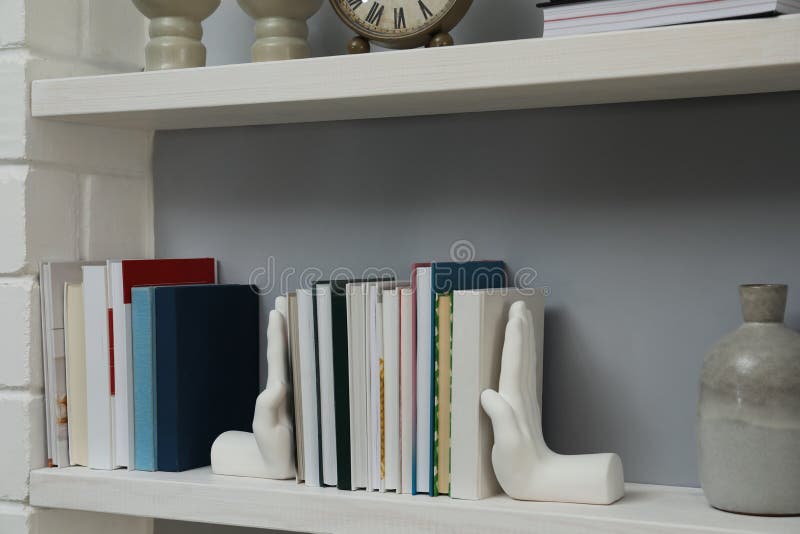 Hand shaped bookends with books on shelf indoors. Interior design