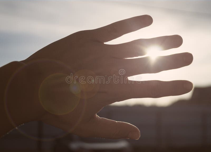 Hand obscuring the sun at sunset with rays making their way through the fingers and sun glare. Hand obscuring the sun at sunset with rays making their way through the fingers and sun glare