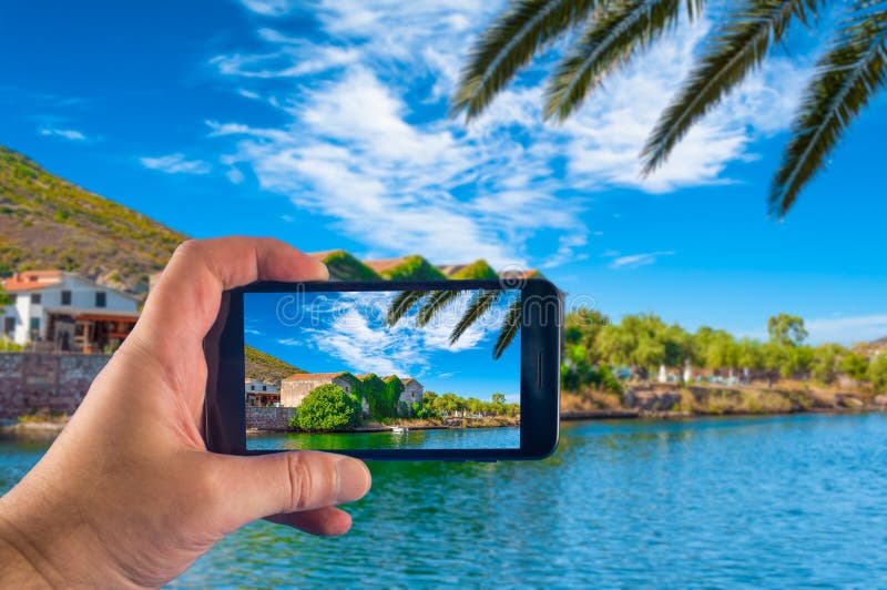 Hand som tar bilden med en smartphone i byn av Bosa, i Sardinia, i sommar royaltyfri foto Hand som tar bilden med en smartphone i byn av Bosa, i Sardinia, i sommar royaltyfri foto