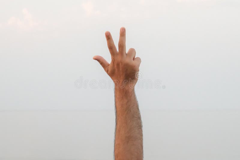 Hand doing, showing number three gesture symbol on bright blue summer sky nature background. Gesturing number 3. Number three in sign language. Third and counting three concepts. 3 finger up. Hand doing, showing number three gesture symbol on bright blue summer sky nature background. Gesturing number 3. Number three in sign language. Third and counting three concepts. 3 finger up