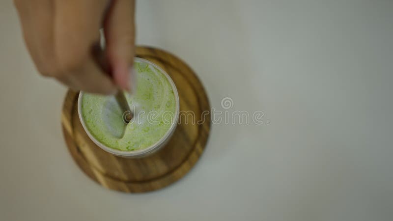 Hand stirring matcha latte in a café setting, showcasing creamy texture and vibrant green color on a wooden coaster royalty free stock photo