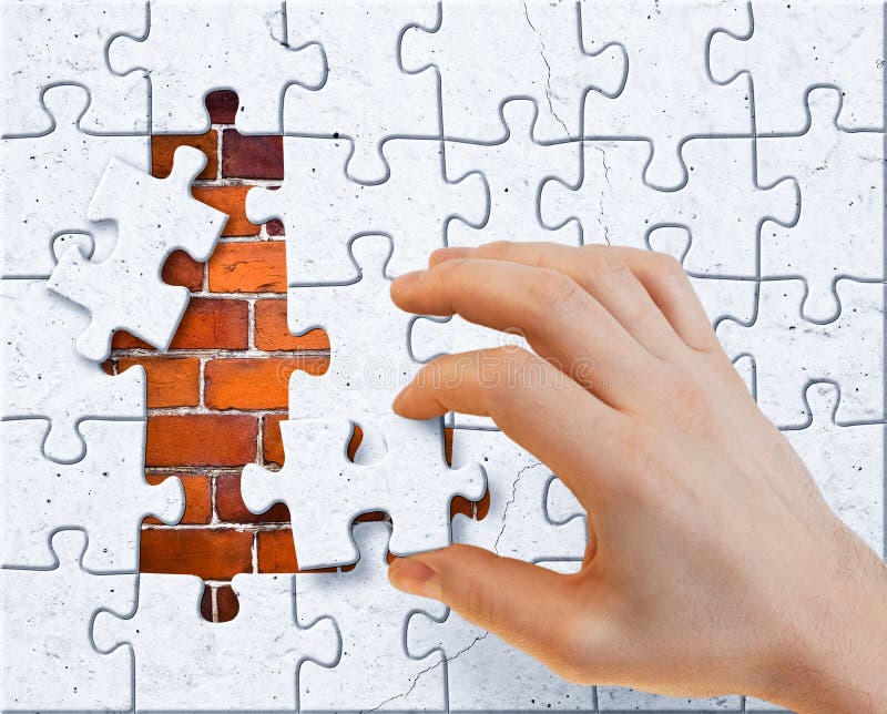 Hand with stucco puzzle pieces covered brick wall